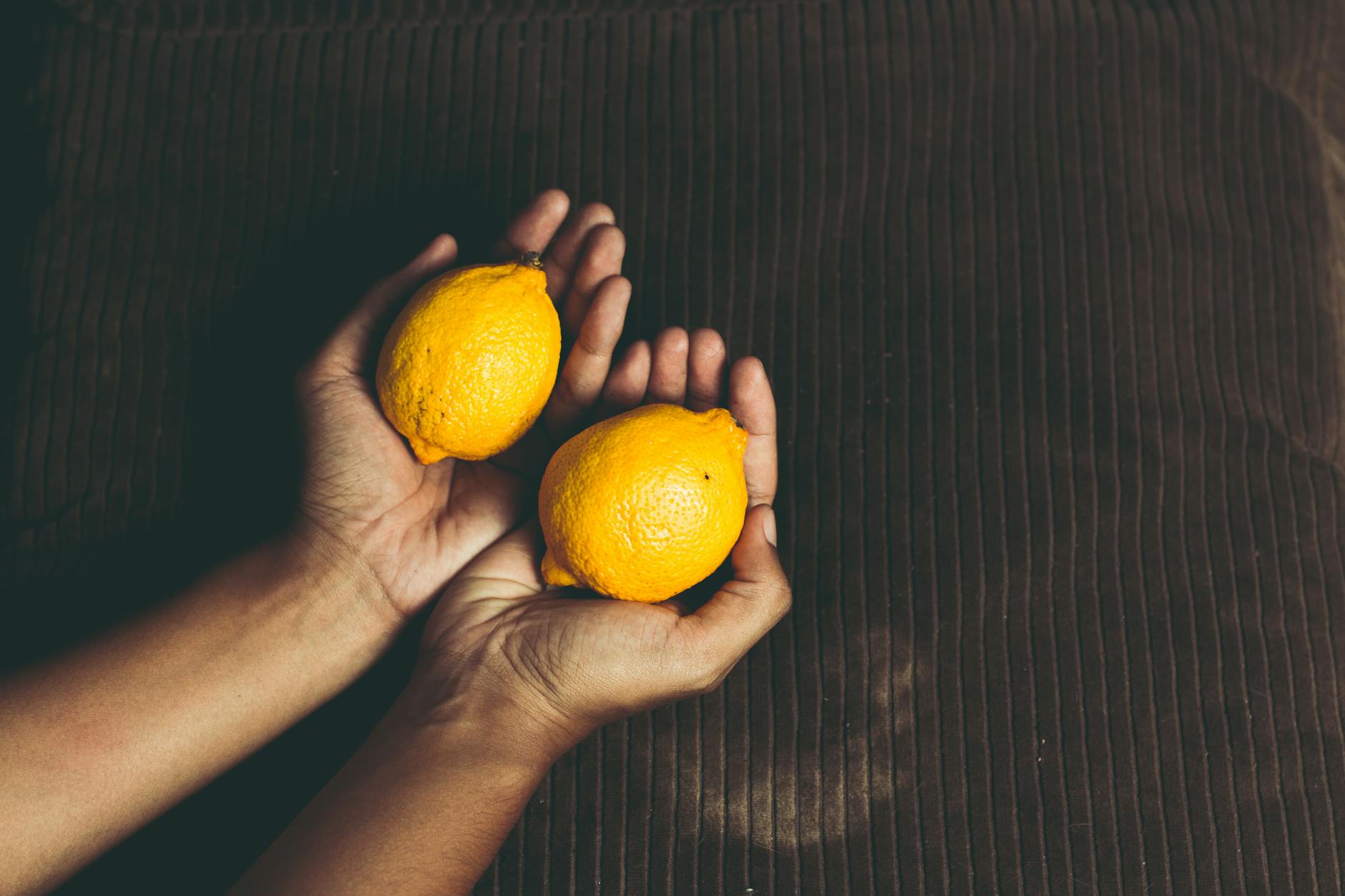 Close-up of two fresh lemons held in cupped hands on a brown surface, symbolizing relief and natural wellness.