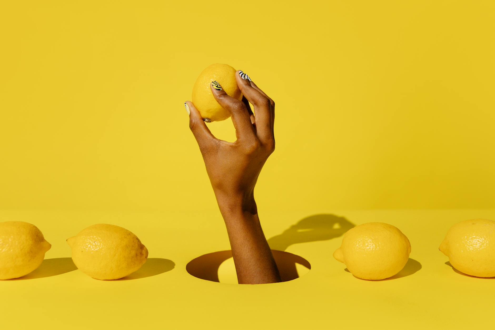 Eine Hand hält eine Zitrone gegen einen leuchtend gelben Hintergrund, symbolisiert Frische und die innovative Technologie des Lemon Vibrators