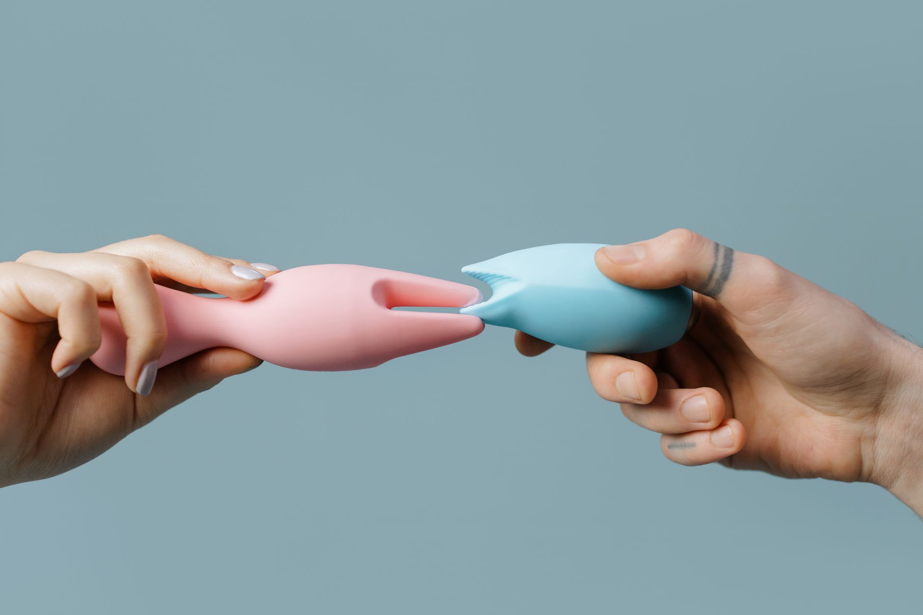 Frau mit Brille hält blaue und rosa Silikon-Vibratoren in nachdenklicher Haltung