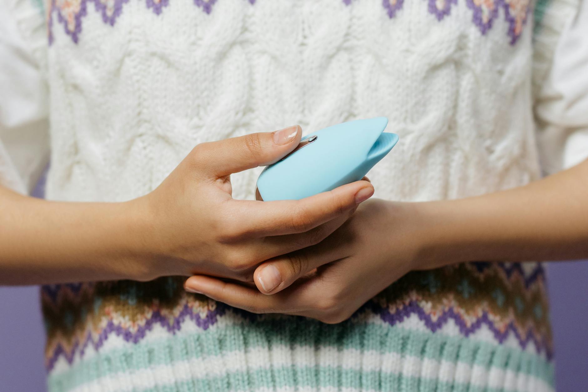 Nahaufnahme einer Hand, die einen blauen persönlichen Massager gegen einen gestrickten Pullover hält.