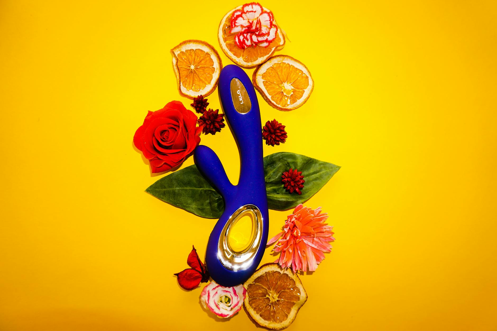Blauer Lemon Vibrator umgeben von Blüten und Orangenscheiben auf gelbem Hintergrund
